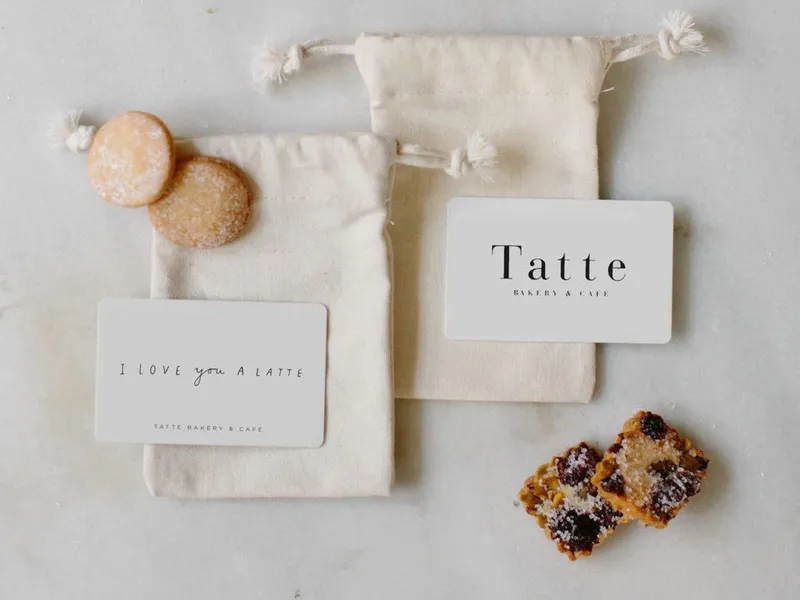 Two tatte gift cards sitting on gift pouches with sugar cookies.